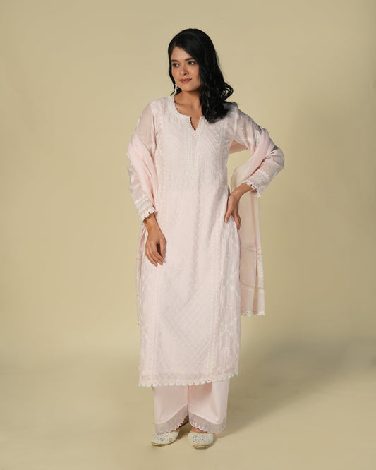 A woman wearing a baby pink chikankari mul chanderi suit set with delicate embroidery, consisting of a kurta and pants.
