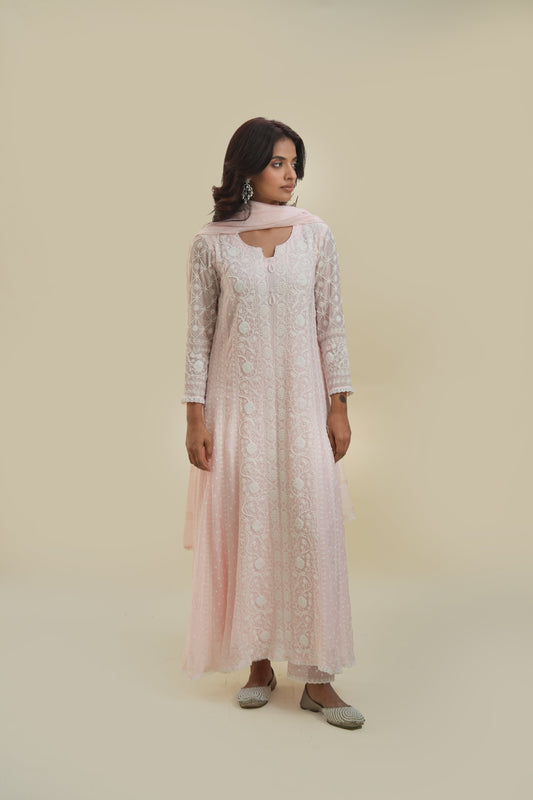 A woman wearing a blush pink Anarkali set with chikankari and mukaish work, paired with a dupatta, standing against a neutral background.