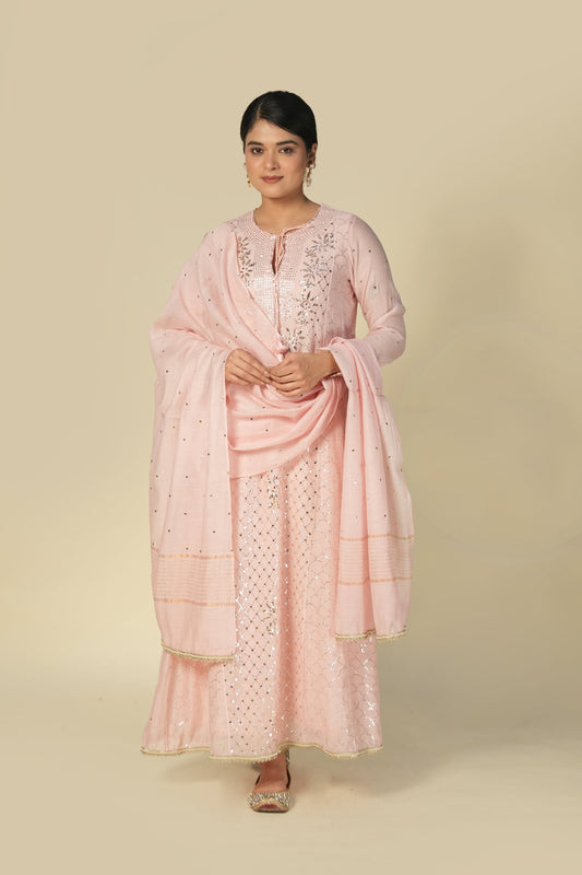 A woman wearing a blush pink mukaish mul chanderi suit set with intricate silver embroidery and a dupatta.