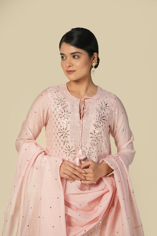 A woman wearing a blush pink mukaish mul chanderi suit set with intricate silver embroidery and a dupatta.