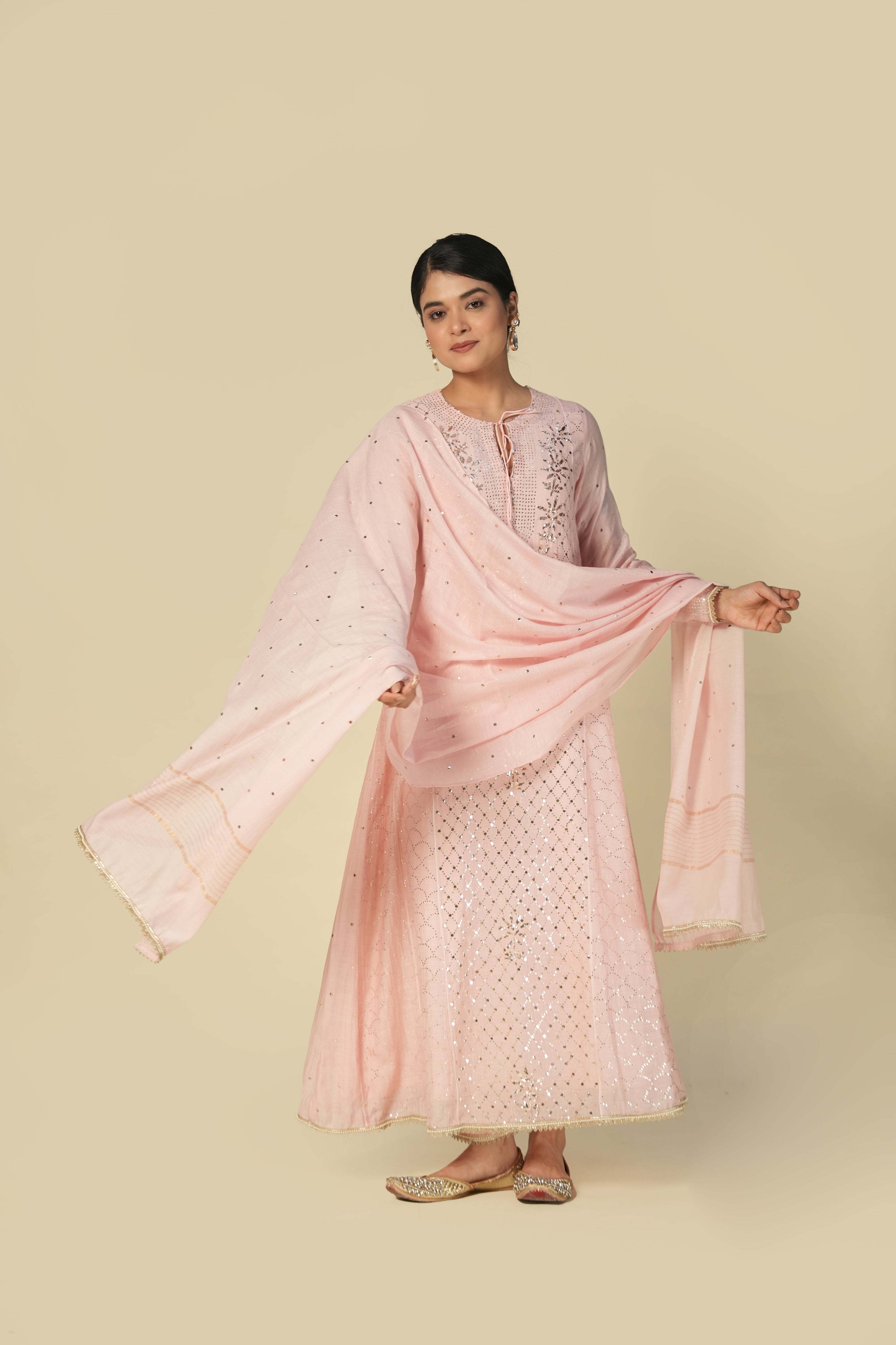 A woman wearing a blush pink mukaish mul chanderi suit set with intricate silver embroidery and a dupatta.