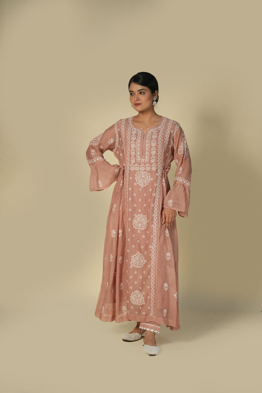 A woman wearing a dusty rose pink chikankari mul chanderi kurta set with intricate embroidery and standing against a beige background.