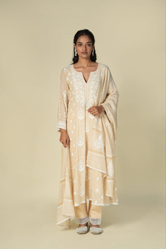A woman wearing a beige straight tissue suit set with chikankari and mukaish work.