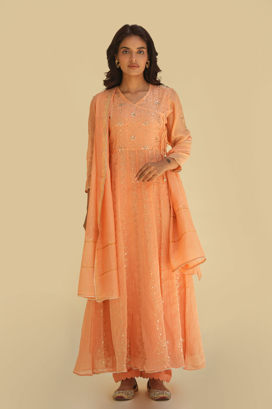 A woman wearing an orange Anarkali suit with detailed embroidery, paired with a dupatta.