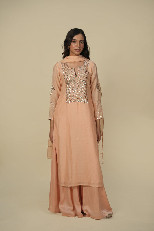 A woman wearing an orange chanderi suit with mukaish work, consisting of intricate embroidery, and paired with a dupatta.