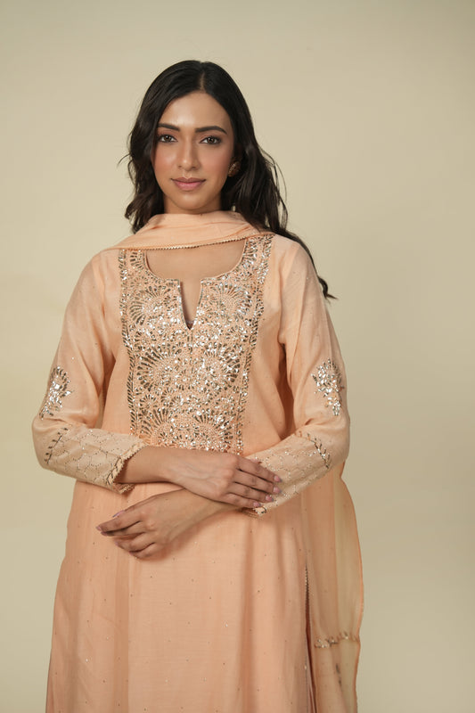 A woman wearing an orange chanderi suit with mukaish work, consisting of intricate embroidery and paired with a dupatta.