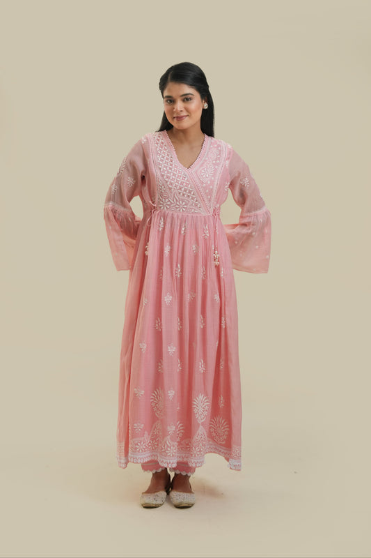 A woman standing against a beige background, wearing a pink Agarkha kurta with detailed embroidery.