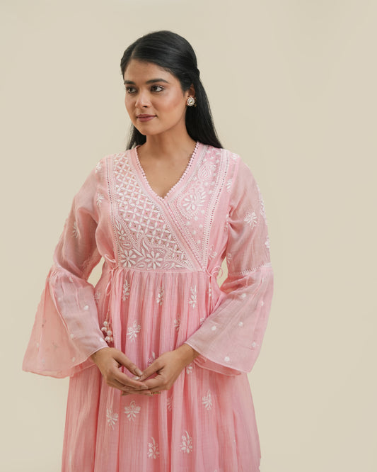 A woman standing against a beige background, wearing a pink Agarkha kurta with detailed embroidery.