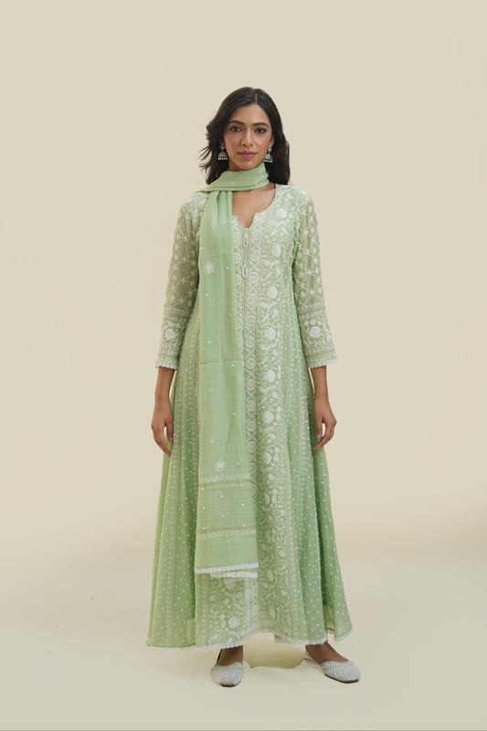 A woman wearing a green anarkali set with chikankari and mukaish work, paired with a dupatta, standing against a neutral background.