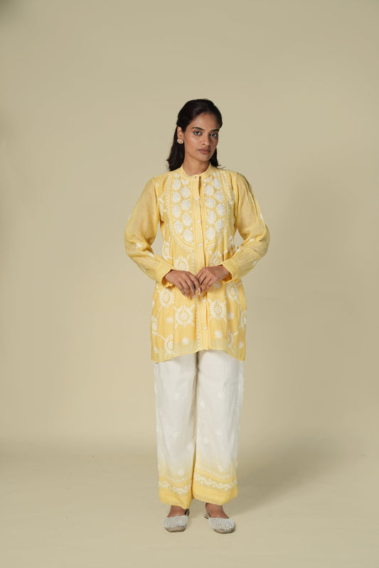 A woman wearing a yellow and white co-ord set with chikankari work on the top, paired with trousers.