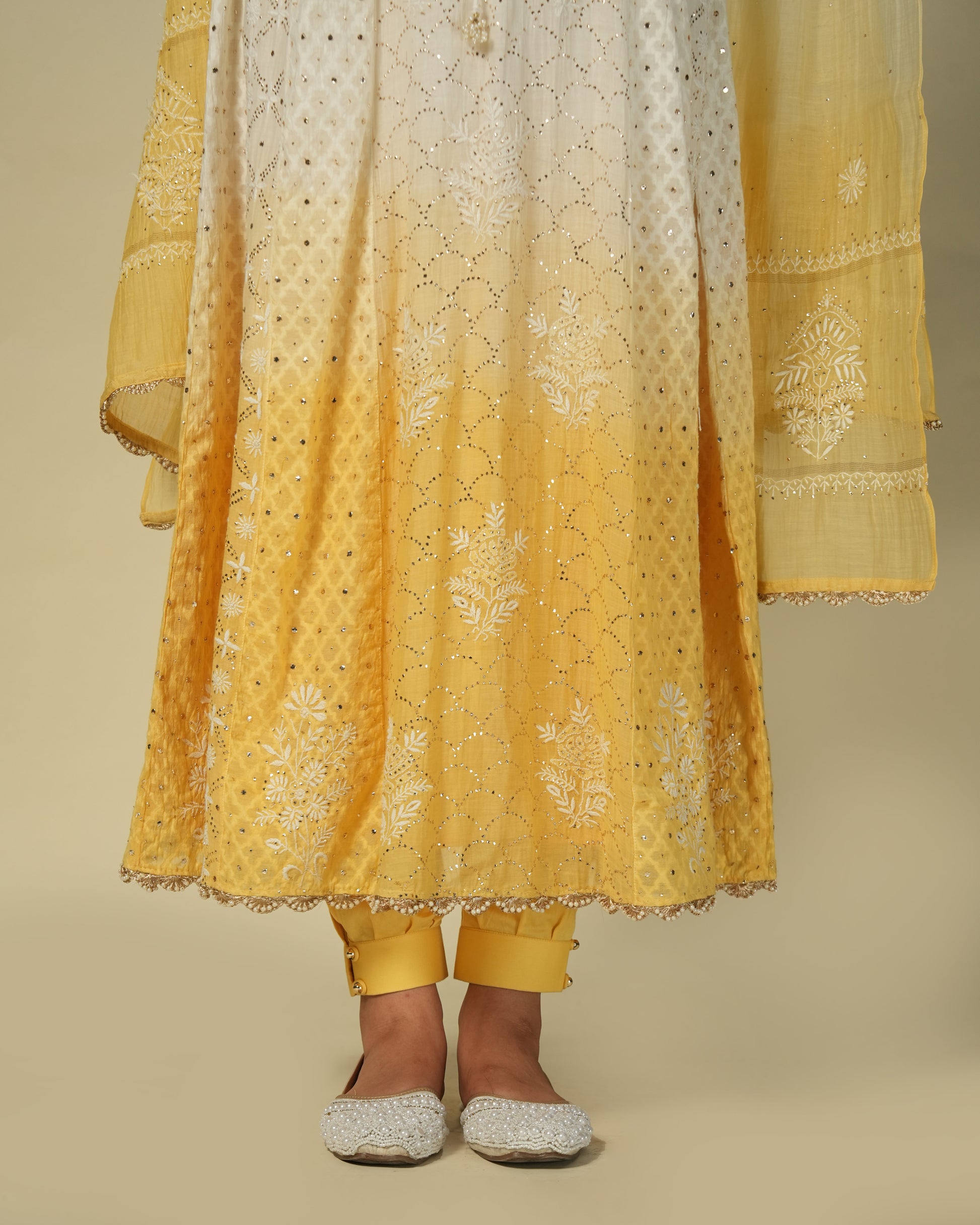 A woman wearing a yellow and white shaded chikankari jacquard cotton anarkali set with intricate embroidery.