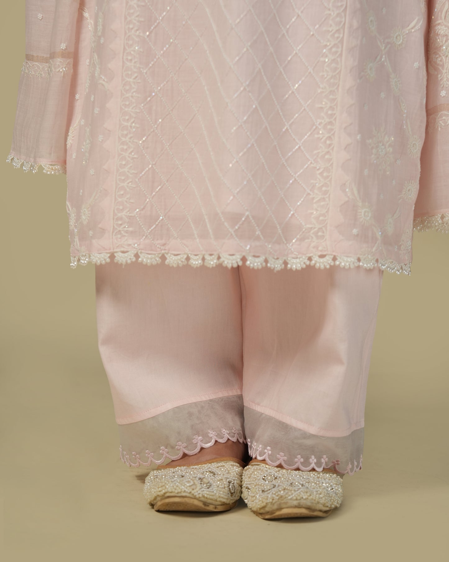 A woman wearing a baby pink chikankari mul chanderi suit set with delicate embroidery, consisting of a kurta and pants.