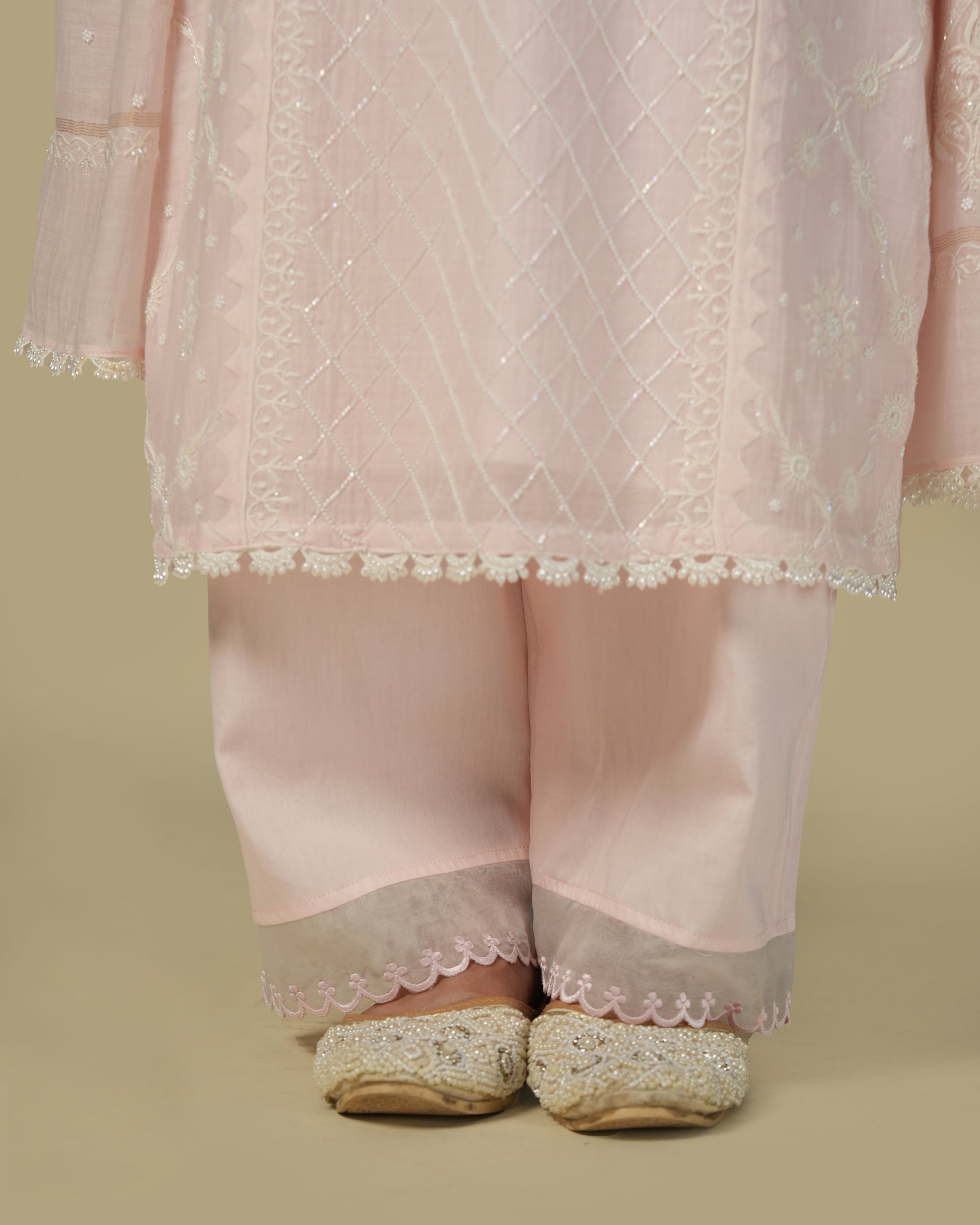 A woman wearing a baby pink chikankari mul chanderi suit set with delicate embroidery, consisting of a kurta and pants.