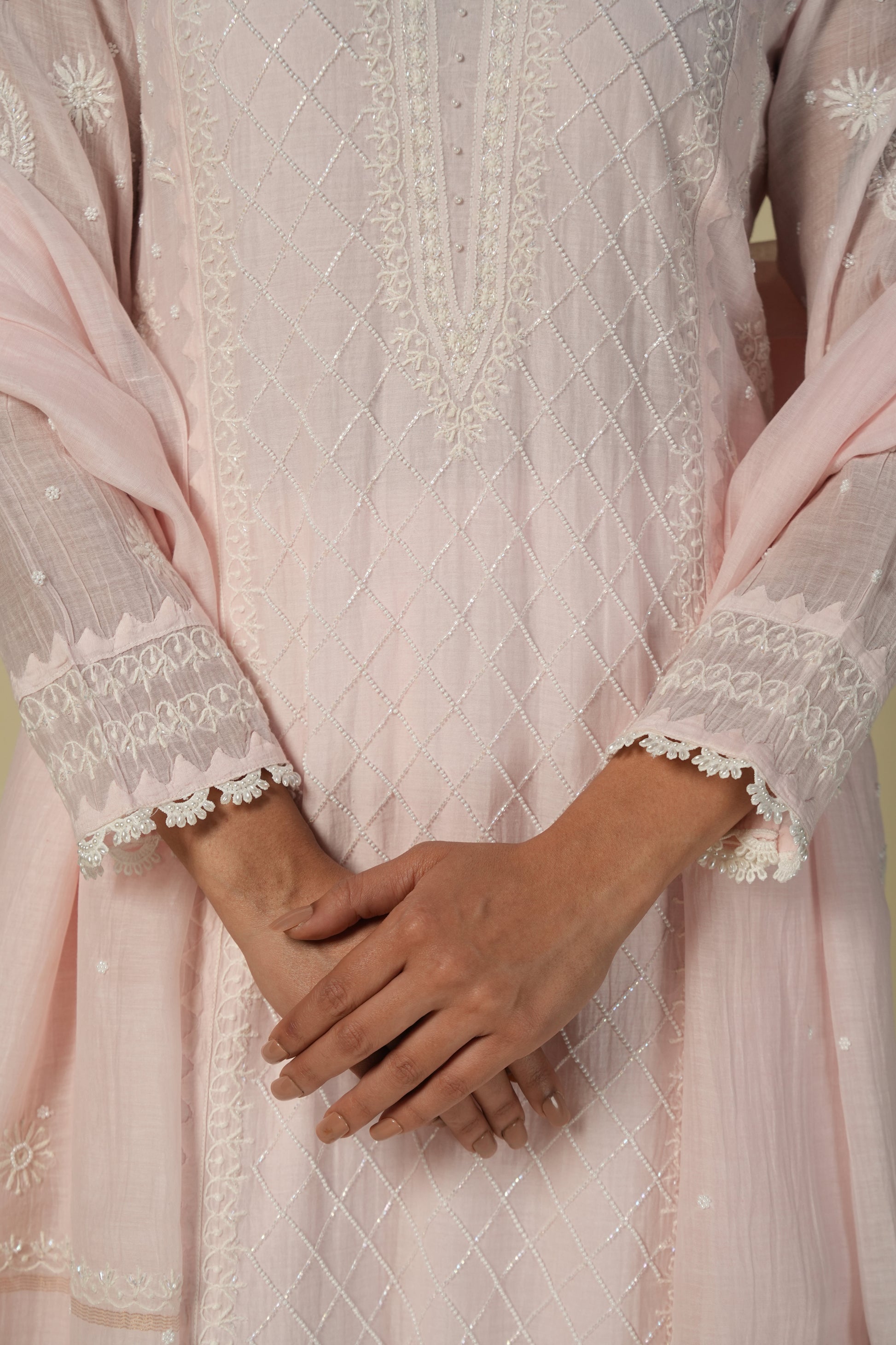A woman wearing a baby pink chikankari mul chanderi suit set with delicate embroidery, consisting of a kurta and pants.