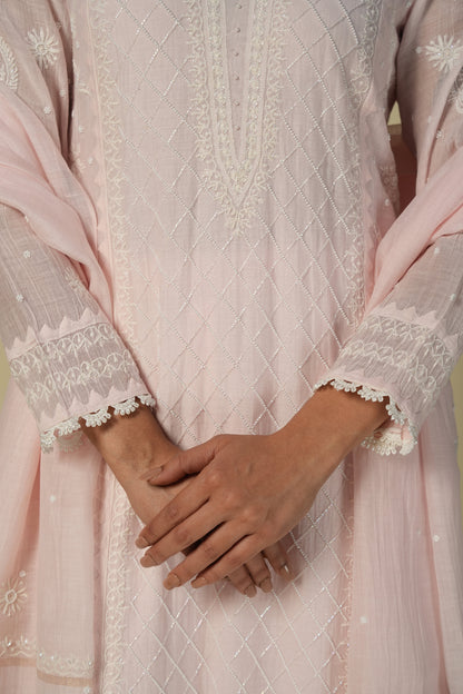A woman wearing a baby pink chikankari mul chanderi suit set with delicate embroidery, consisting of a kurta and pants.