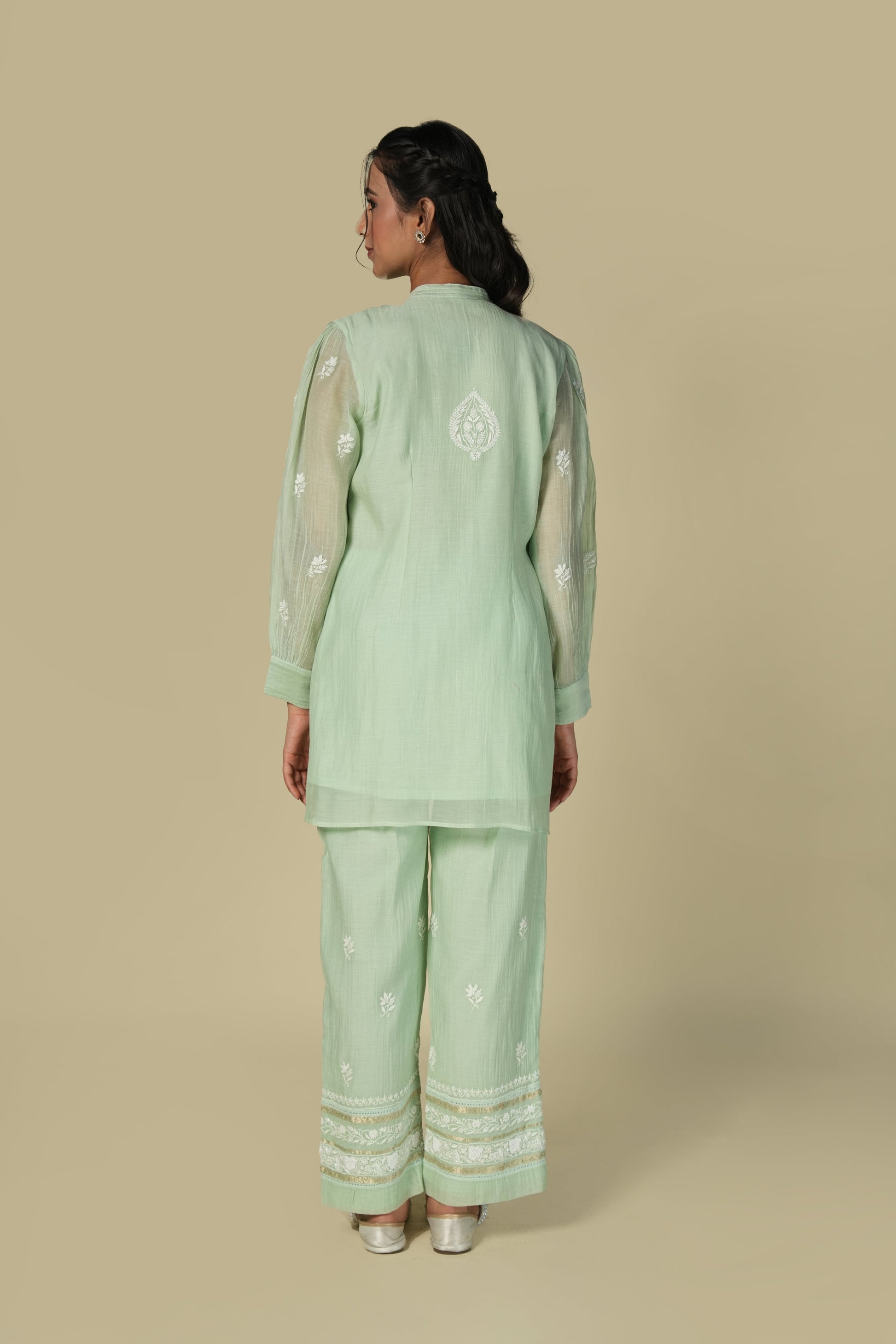 A woman standing and modeling a green mul co-ord set with chikankari work, consisting of a tunic and pants.